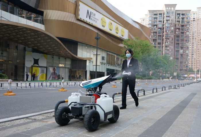 4월 12일(현지시간) 중국 후베이성 우한에서 마스크를 쓴 한 여성이 로봇을 작동 시켜 거리를 소독하고 있다. AP/뉴시스
